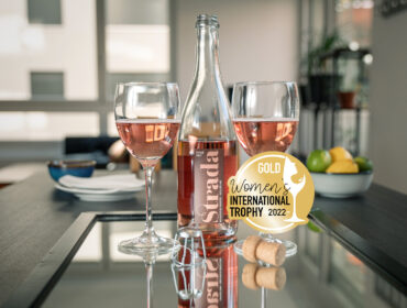 Der durch die Women's International Trophy 2022 mit Gold ausgezeichnete Schaumwein Strada Rosé steht auf einen Glastisch